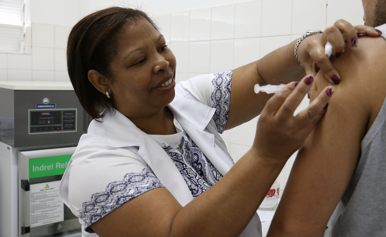 Imagem mostra enfermeira sorrindo aplicando a vacina contra a Covid.