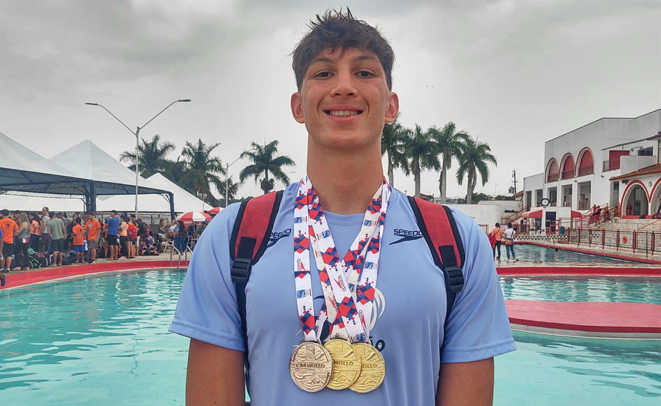 Foto do nadador Daniel Sala Bordin, em frente a uma piscina, exibindo suas medalhas