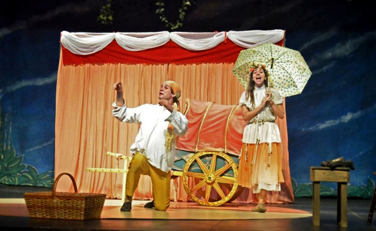 Foto de dois atores no palco durante exibição do espetáculo "Libel e o Palhacinho"