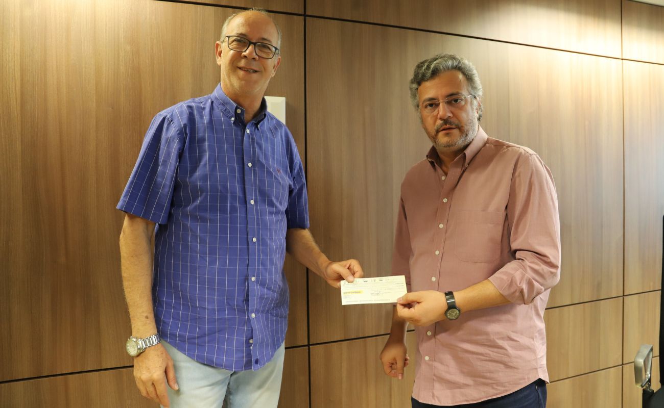 Fotografia mostra o presidente da Câmara de Vereadores, Mané da Saúde, entregando o cheque ao prefeito Guilherme Gazzola