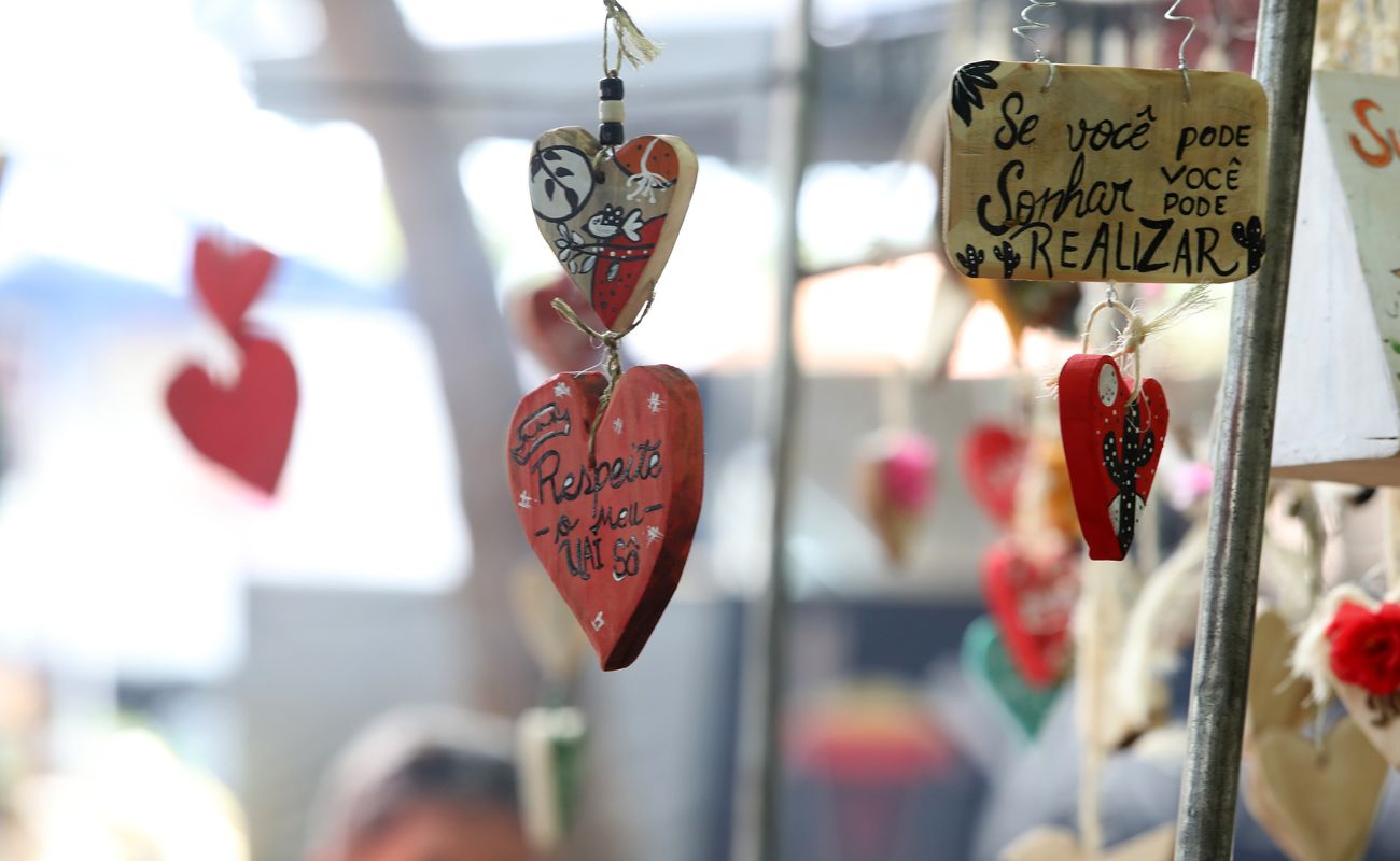 Imagem mostra uma das barracas da feira ecoart, com a exposição de duas placas em formatos de coração e uma retangular em madeira, com frases motivacionais.