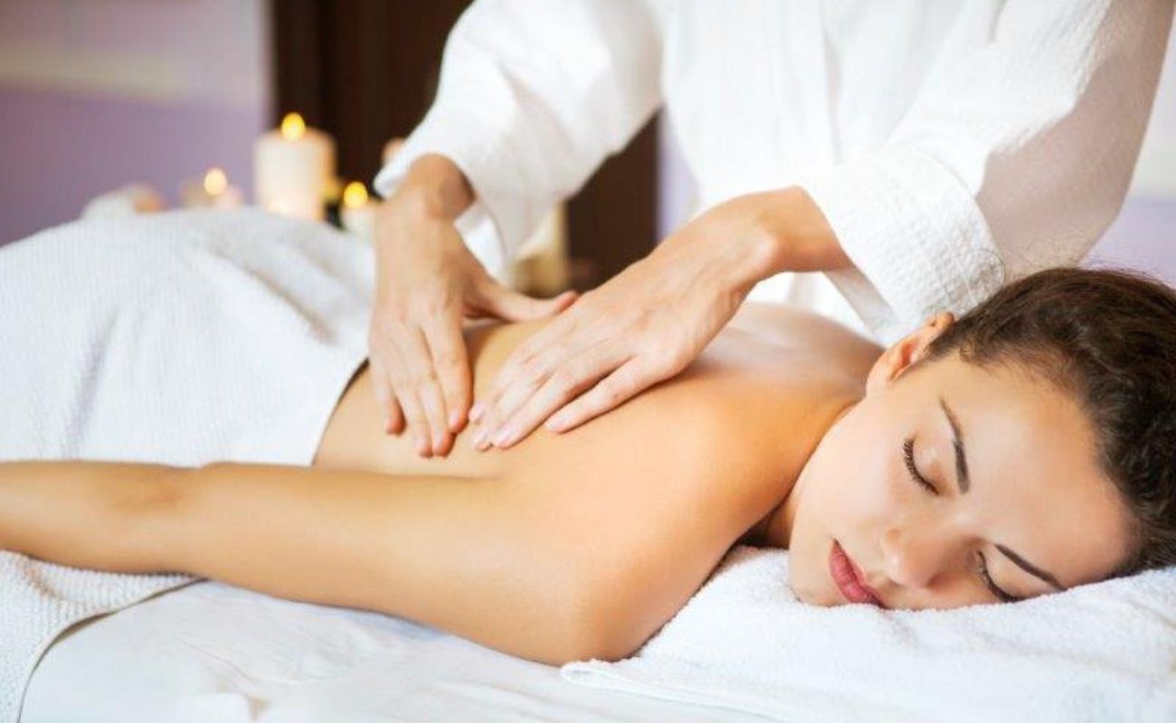 Imagem mostra mulher jovem recebendo massagem relaxante. O curso de massagem relaxante será oferecido conforme informado.