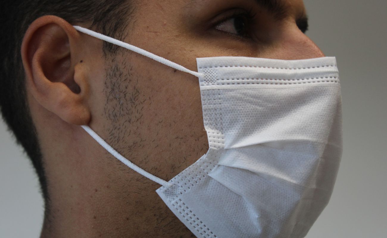 Imagem mostra o rosto de um homem de perfil, usando máscara de proteção branca.