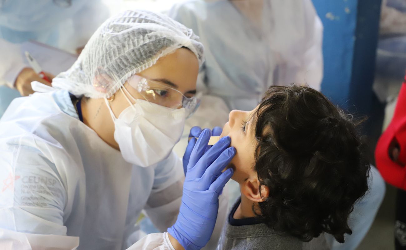 Imagem mostra uma criança passando por avaliação odontológica com uma profissional da área.