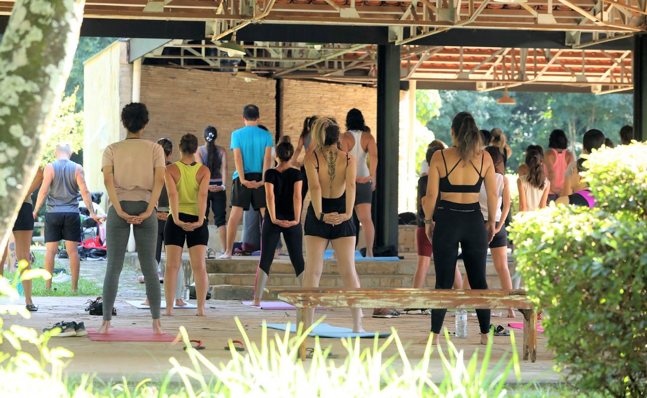 Imagem mostra pessoas de costas com os braços posicionados para trás. Trata-se de um dos exercícios praticados na aula de yoga livre.