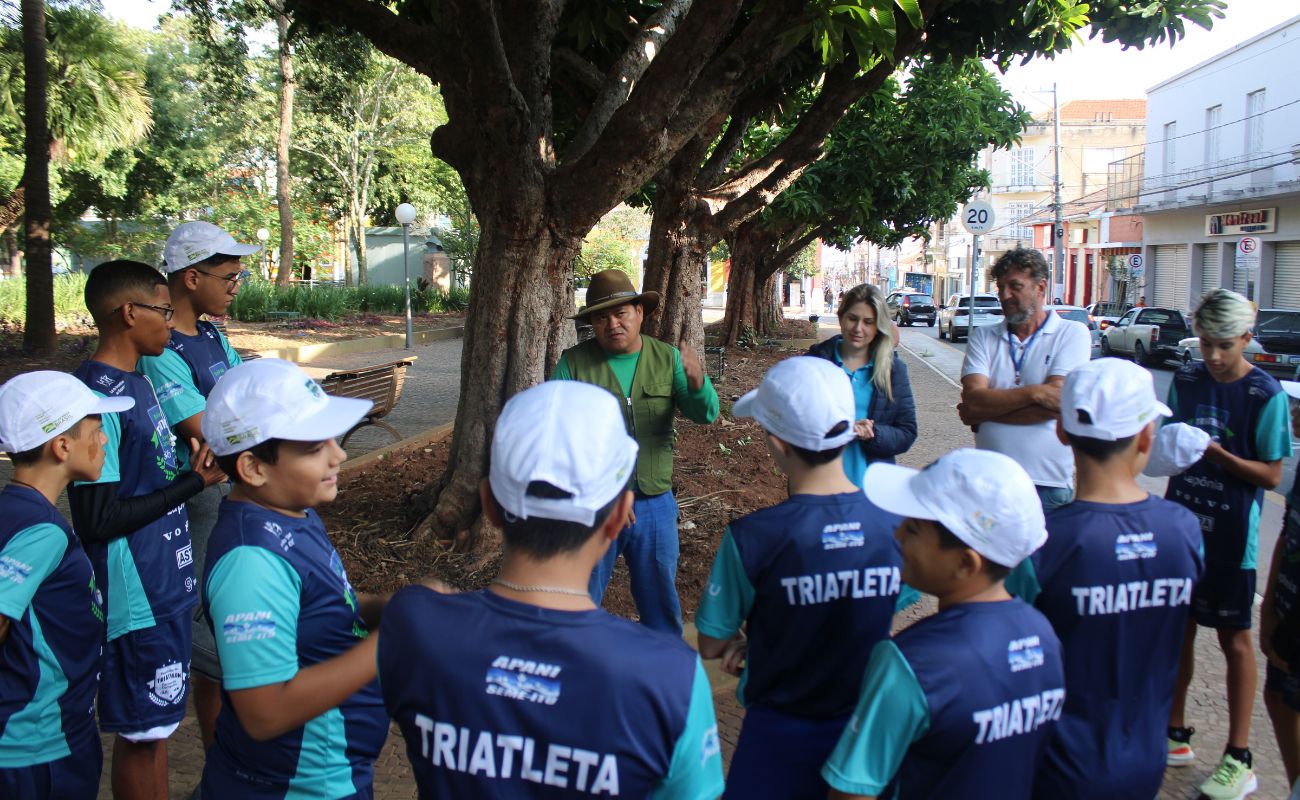 Imagem mostra os atletas de costas ouvindo as orientações sobre o plantio da equipe da Secretaria Municipal de Meio Ambiente.