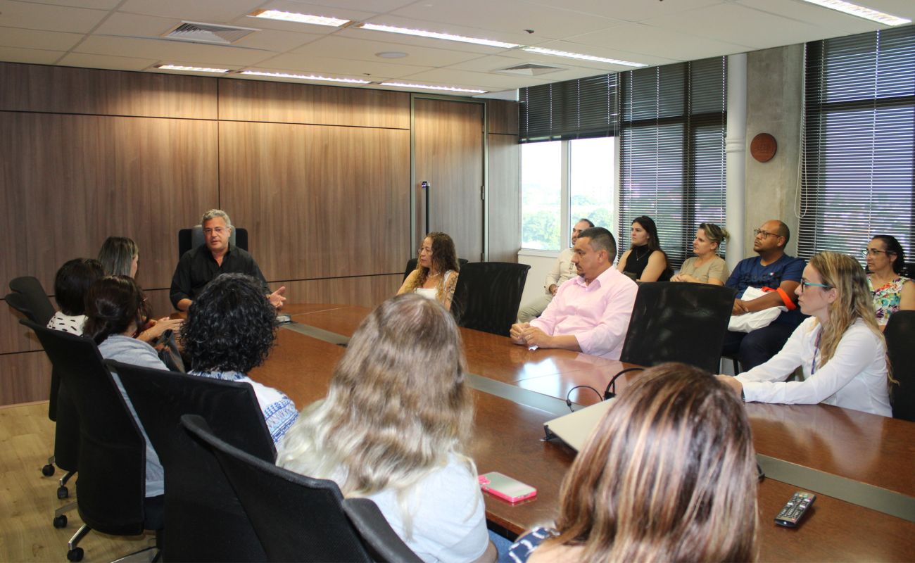 Imagem mostra o prefeito Guilherme Gazzola e autoridades municipais junto aos novos servidores, sentados ao redor de uma mesa, na sala de reuniões do gabinete.