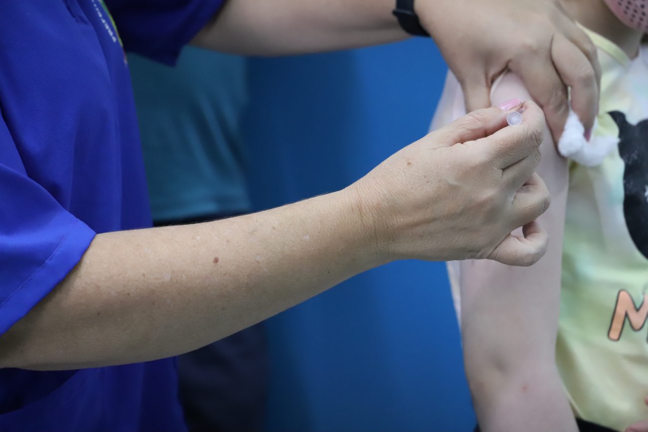 Imagem mostra em close uma enfermeira realizando a aplicação da vacina em uma pessoa.
