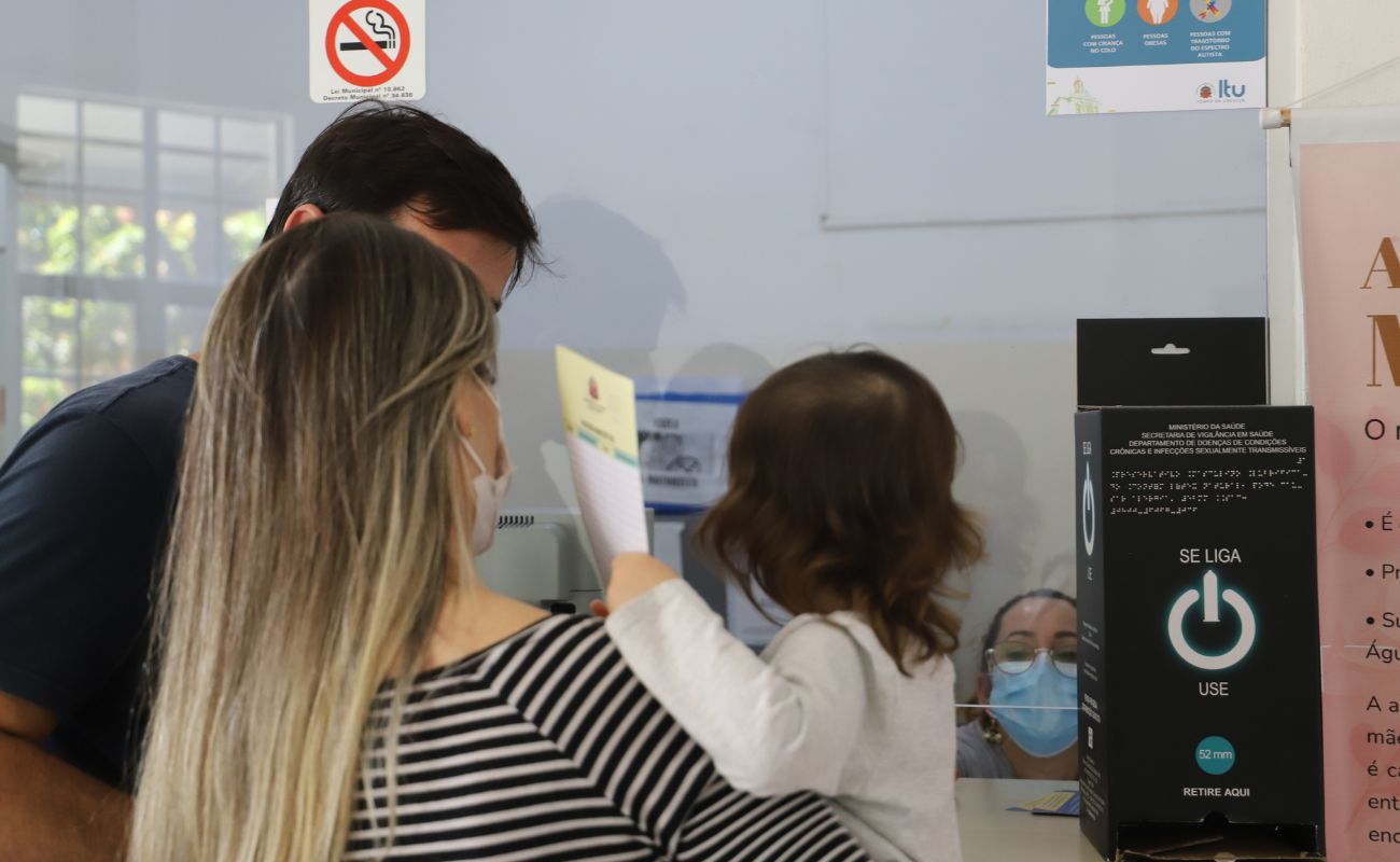 Imagem mostra dois adultos com uma criança no colo da mãe, sendo atendidos em uma das unidades básicas de saúde para completar o esquema vacinal de prevenção contra a Covid.