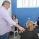 Imagem mostra o prefeito Guilherme Gazzola com a mão direita tocando o ombro de uma munícipe que está sentada sendo atendida por uma servidora da equipe da Saúde. A ação faz parte do Programa Zera Fila da Saúde.