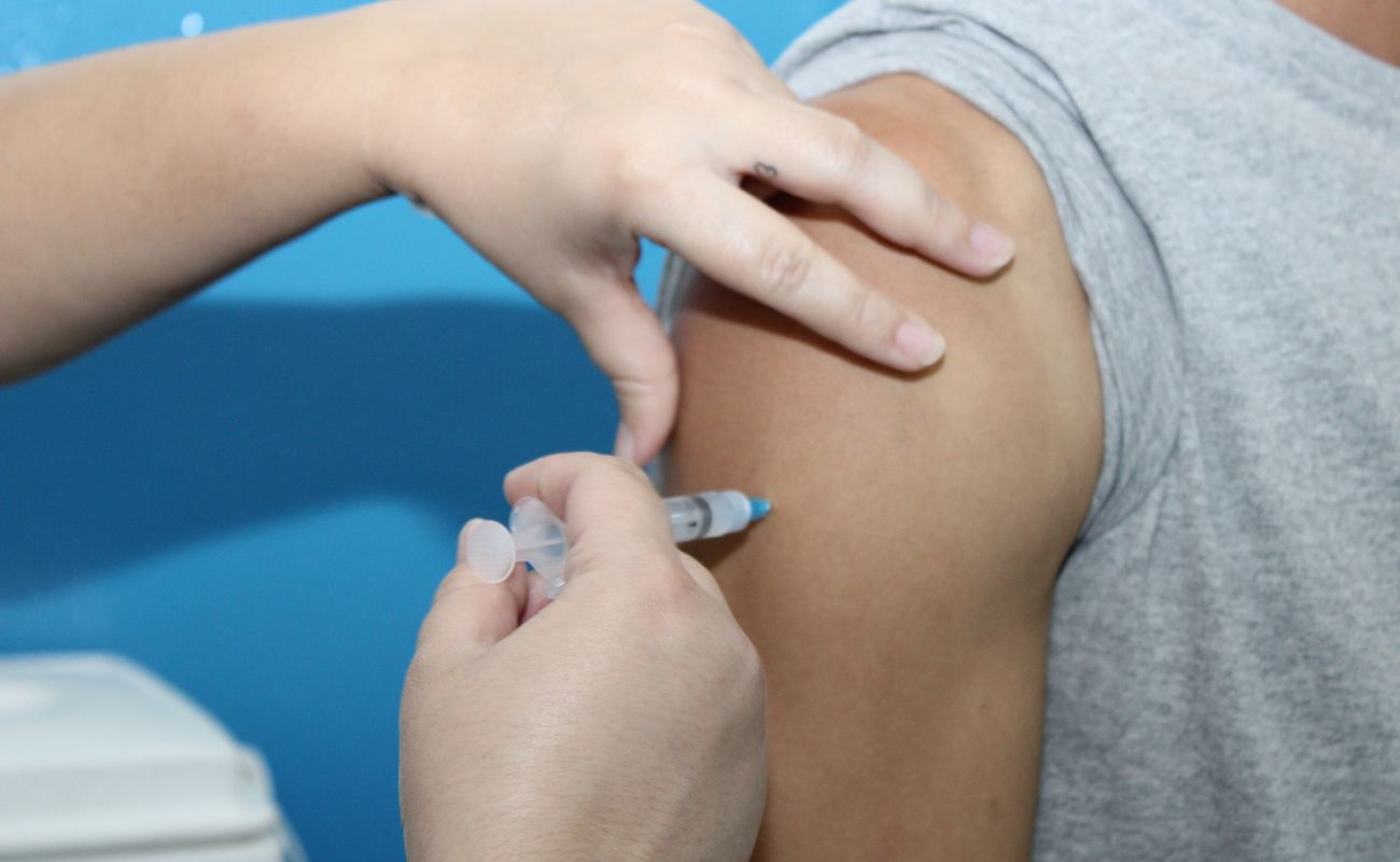 Imagem mostra o braço direito de um homem e as mãos de uma enfermeira em momento de aplicação da segunda dose da vacina contra a Covid
