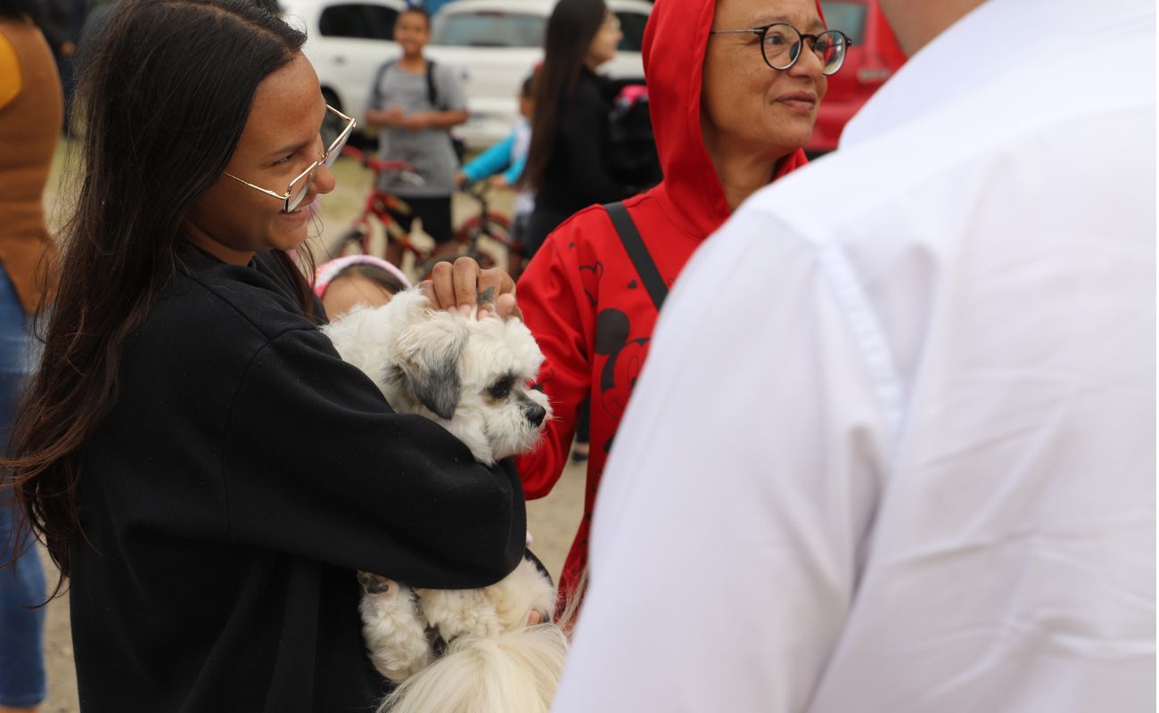 Imagem mostra duas mulheres sendo uma delas carregando um cachorro branco com orelhas na cor cinza, no dia do Mutirão da Castração na Cidade Nova