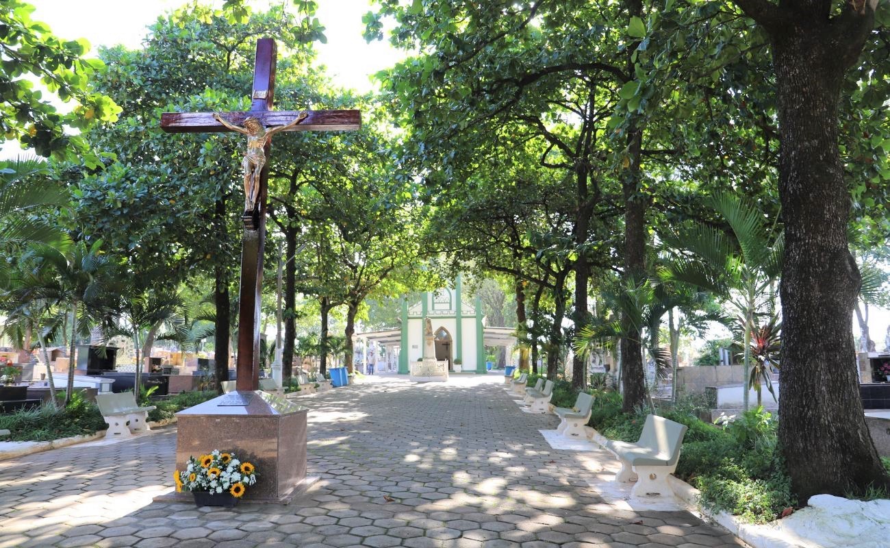Imagem mostra a entrada do cemitério municipal, com uma grande imagem de Jesus na cruz e árvores ao redor, que neste final de semana conta com programação alusiva em comemoração ao dia dos pais