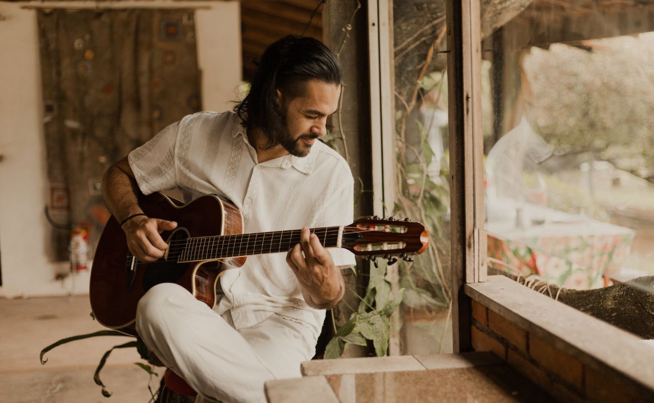 Imagem mostra o cantor Everson Nunes sentado com roupas brancas, tocando seu violão.