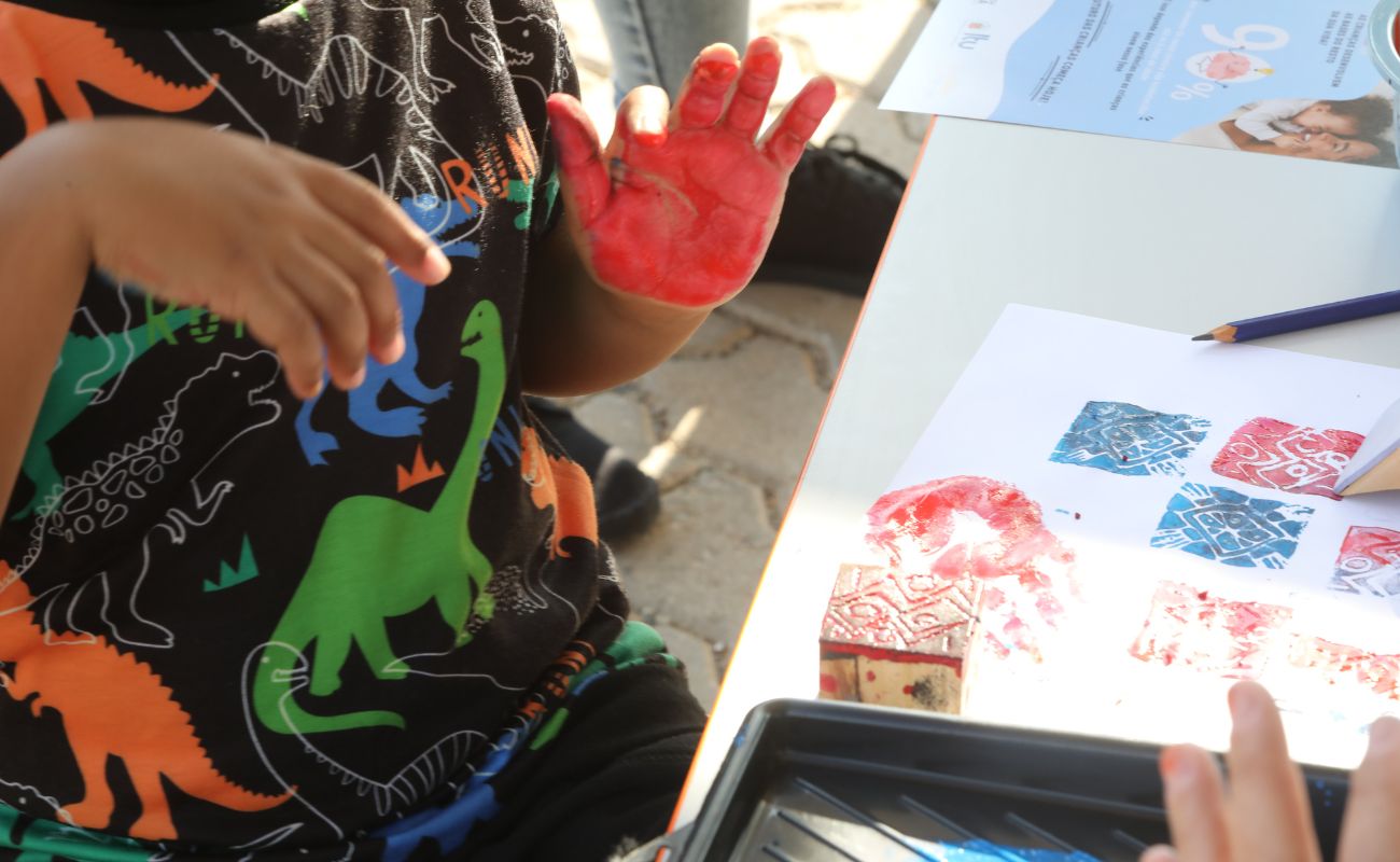 Imagem mostra em foco as mãos de uma criança pintada de vermelho em uma das brincadeiras na manhã das crianças, um evento que faz parte da Semana da Primeira Infância realizada no ano anterior.