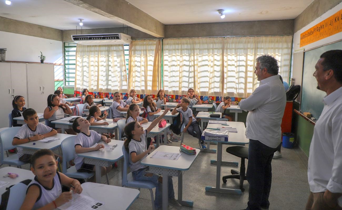 Imagem mostra o prefeito Guilherme Gazzola conversando com alunos de uma sala de aula da rede municipal, que recebeu o ar condicionado junto as creches.