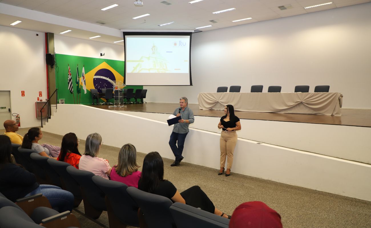Imagem mostra o Prefeito Guilherme Gazzola e a chefe de gabinete Michelle Campanha a frente do auditório conversando com os novos servidores.