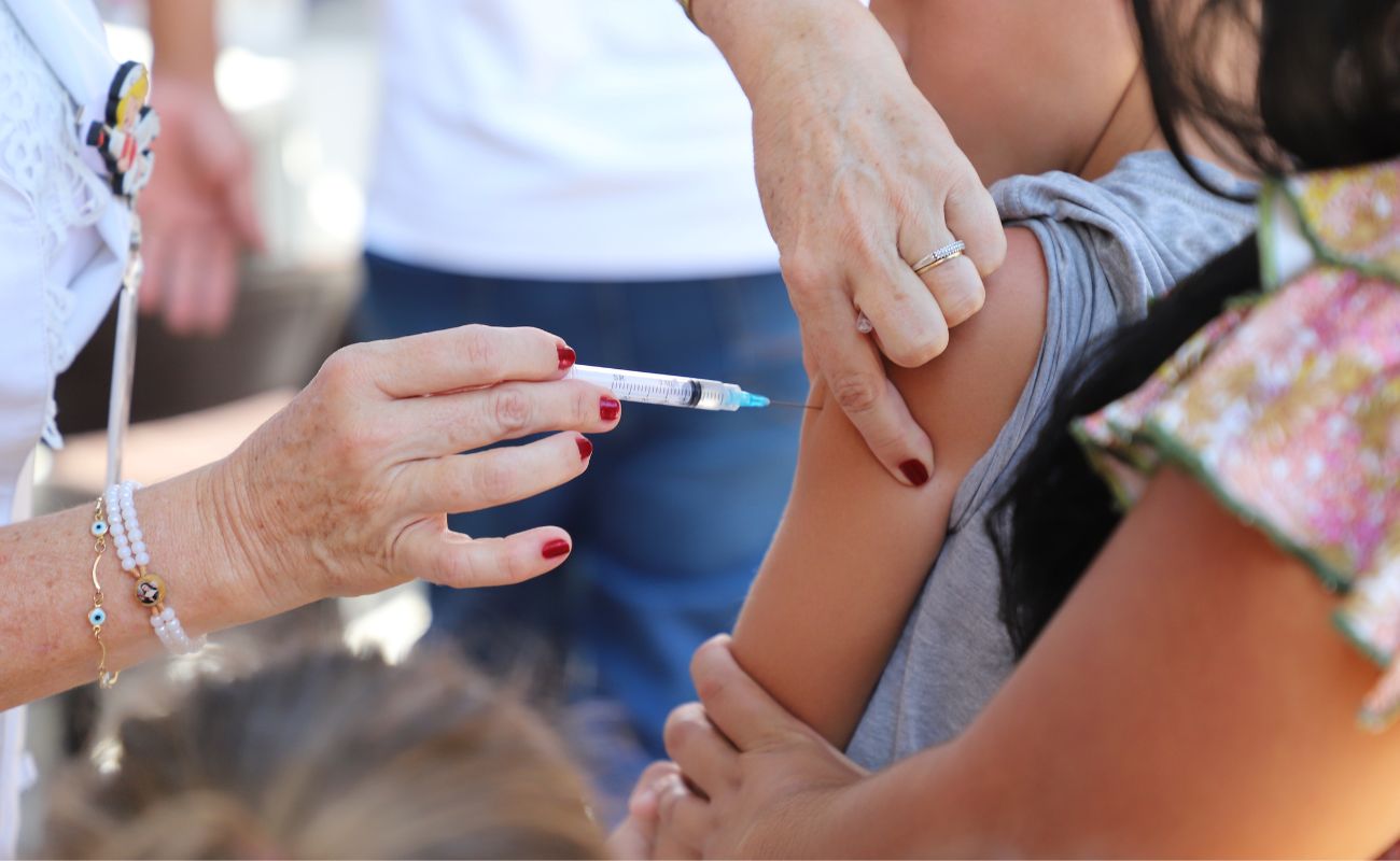Imagem mostra um braço de uma criança em foco, recebendo dose de vacina em último evento Caravana Social. O próximo evento acontece no sábado 24/02 no antigo cemitério Pedra da Paz