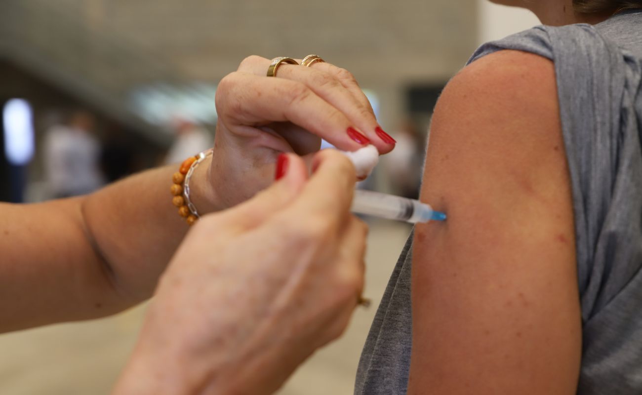 Imagem mostra em foco um braço recebendo uma vacina.