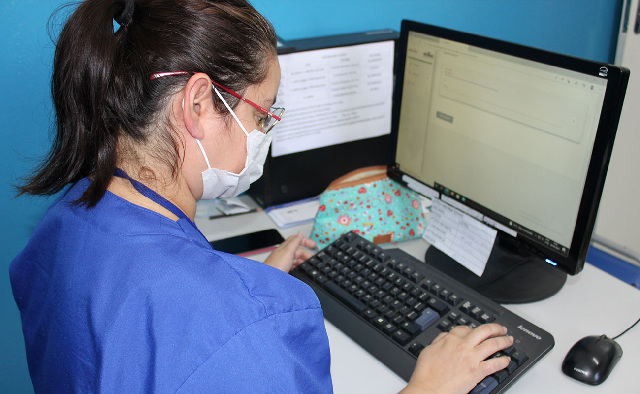 Imagem mostra enfermeira sentada, se utilizando de computador em vacinação contra a gripe.