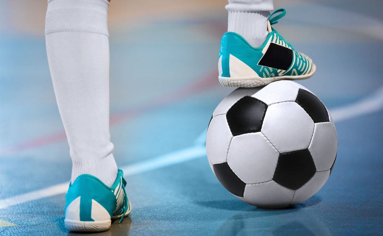Imagem de pés de um atleta, um dos pés está apoiado em uma bola de futebol