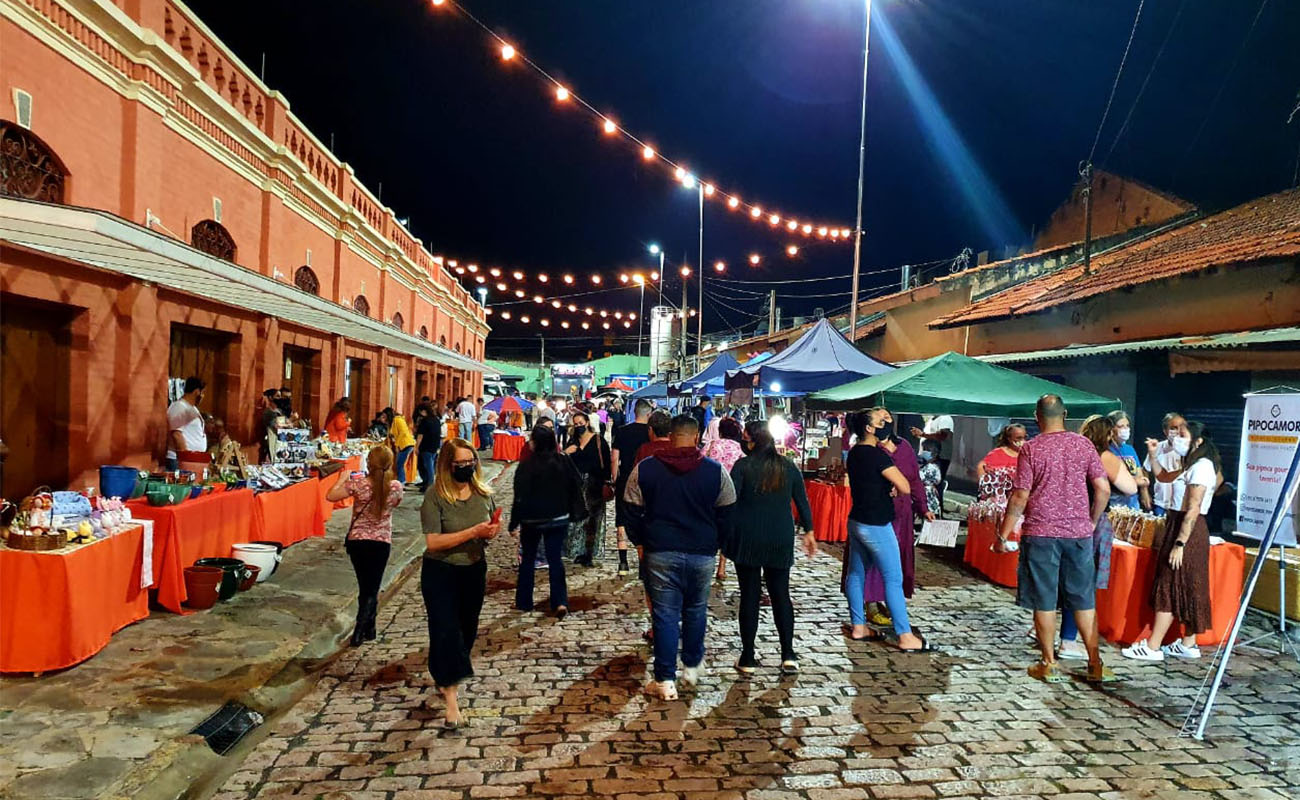Foto da feira noturna com várias pessoas a noite prestigiando as barracas com comerciantes