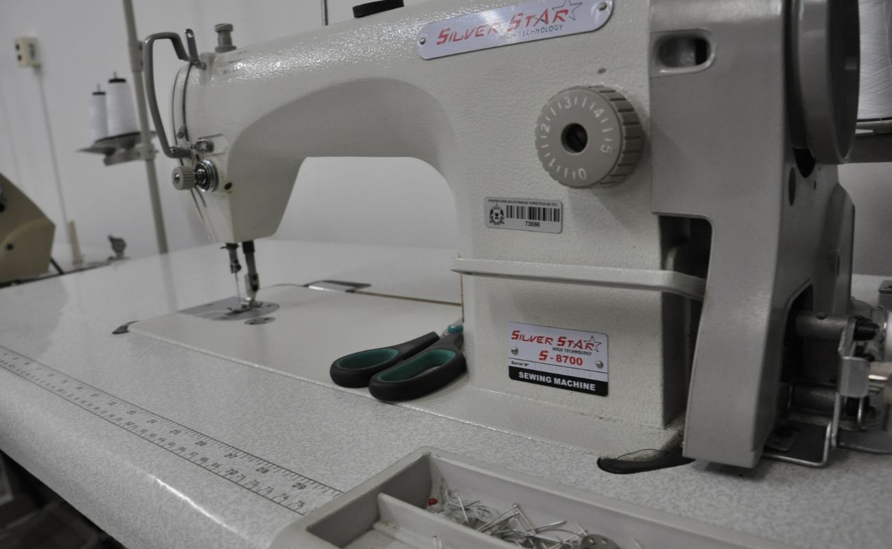 Foto preta e branca mostra uma máquina de costura junto a uma tesoura.