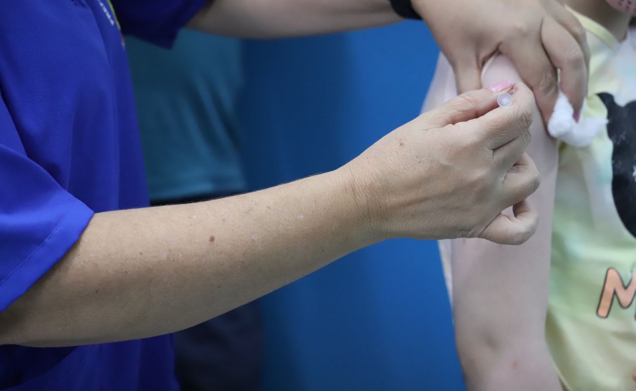 Imagem mostra os braços de um profissional de saúde aplicando a vacina contra Covid em uma cidadã