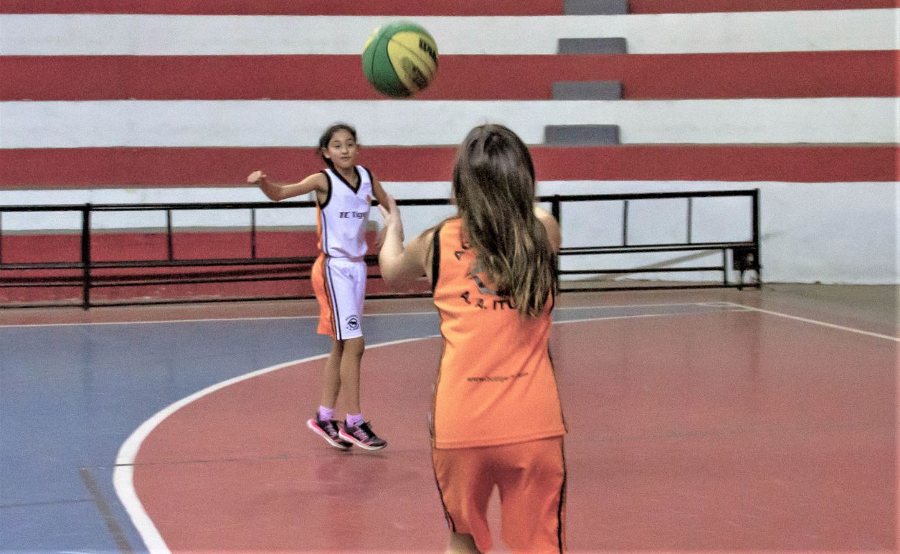 Imagem mostra duas meninas jogando basquete em uma quadra. As inscrições para aulas gratuitas das escolinhas de esportes estão abertas.