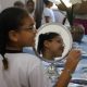 Imagem mostra menina com seu óculo sem frente ao espelho, olhando para a lateral. A referida é beneficiada pelo Projeto Ver + Educa