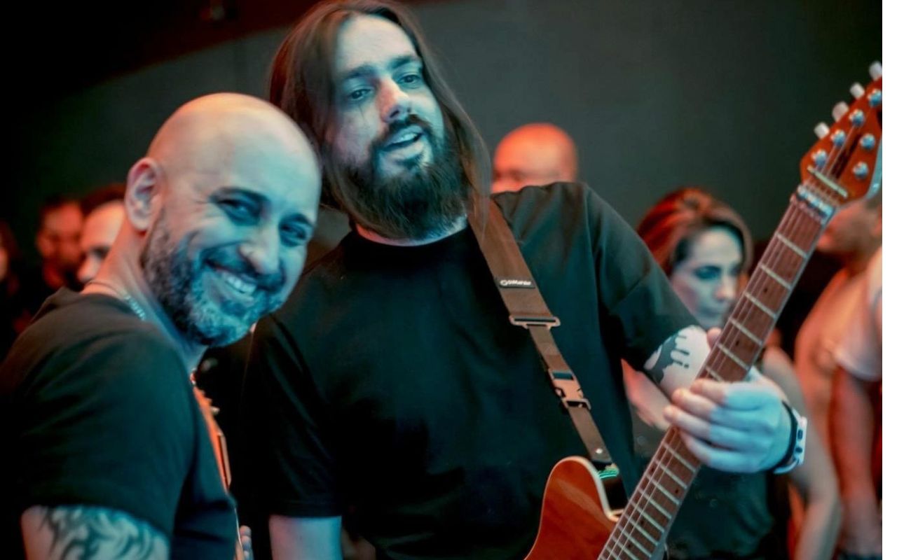 Imagem mostra dois integrantes do grupo musical de pop rock Jack a 3, ambos sorrindo e um deles segurando uma guitarra.
