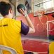 Imagem mostra menino de costas com camiseta amarela e uma bola preta nas mãos, arremessando na cesta de basquete no Festival Paralímpico anterior.