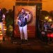 Imagem mostra o palco no dia do evento Empório Cultural, com o cantor Cantor Grilo junto a dois músicos, sendo um deles tocando bateria e outro guitarra.