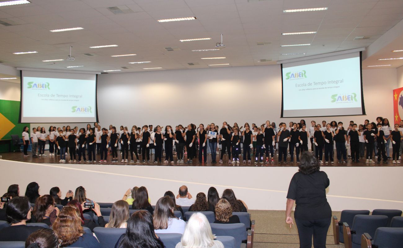Imagem mostra alunos se apresentando em palco do auditório do paço municipal no evento I Fórum de Educação das Escolas Municipais de Tempo Integral.