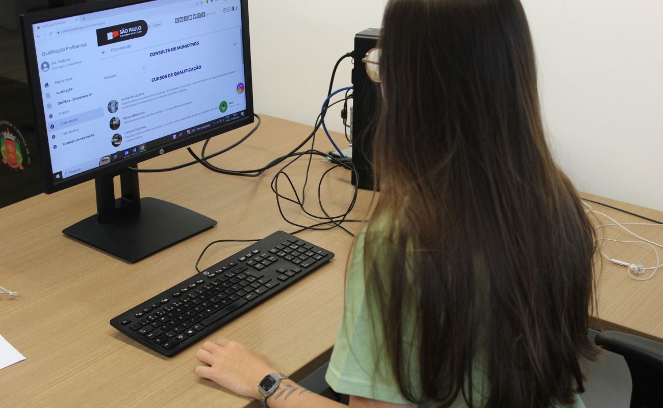 Imagem mostra mulher de costas sentada olhando para uma tela de computador os cursos do Via Rápida