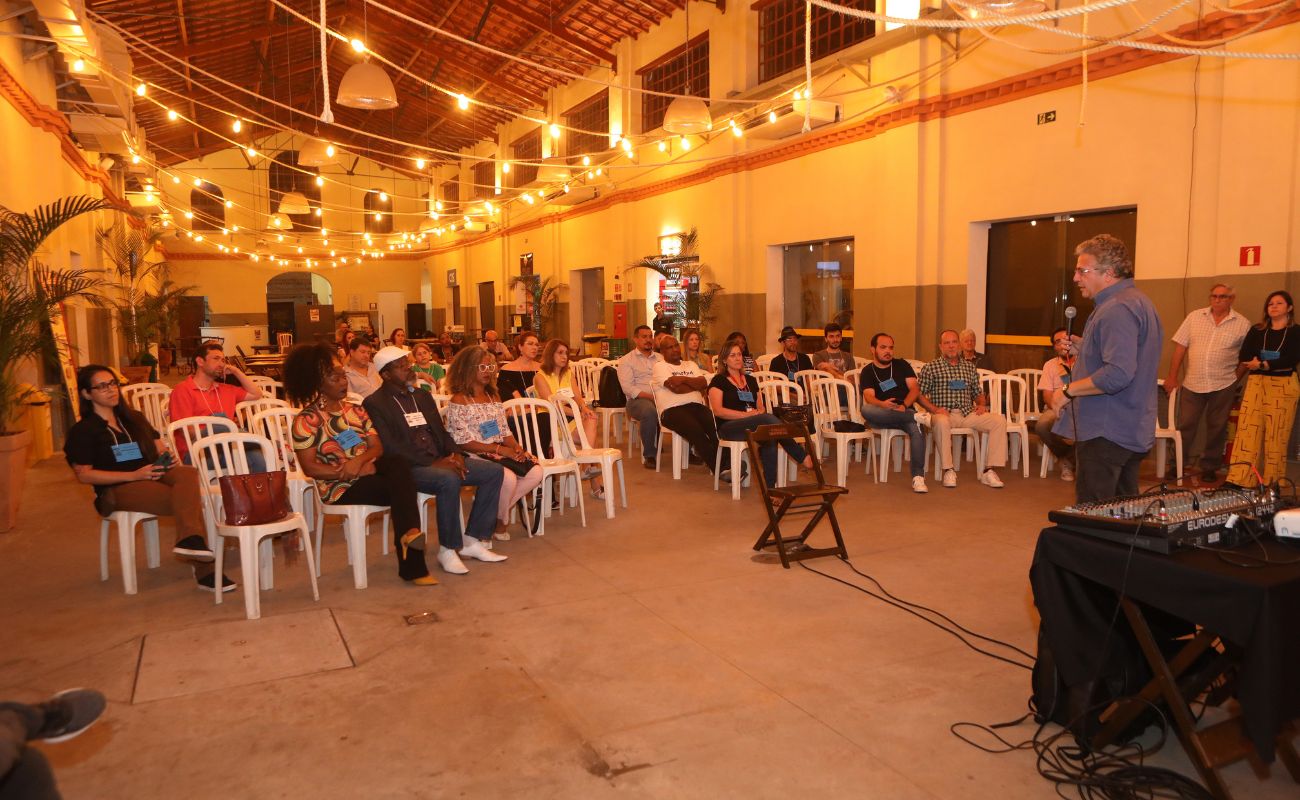 Imagem mostra o prefeito Guilherme Gazzola em pé falando ao microfone com cerca de 70 pessoas, que participaram da Conferência Municipal de Cultura