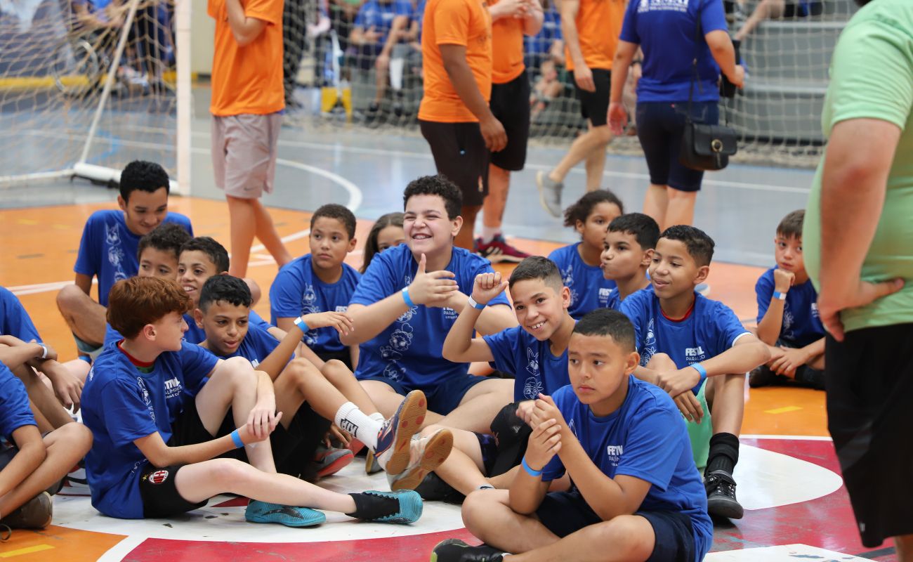 Imagem mostra crianças que participaram do Festival Paralímpico, todas uniformizadas sentadas e quadra de futebol de salão