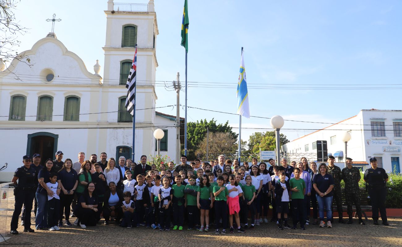 Imagem mostra um grupo de alunos posicionados em frente a bandeira nacional em momento de hastiamento.