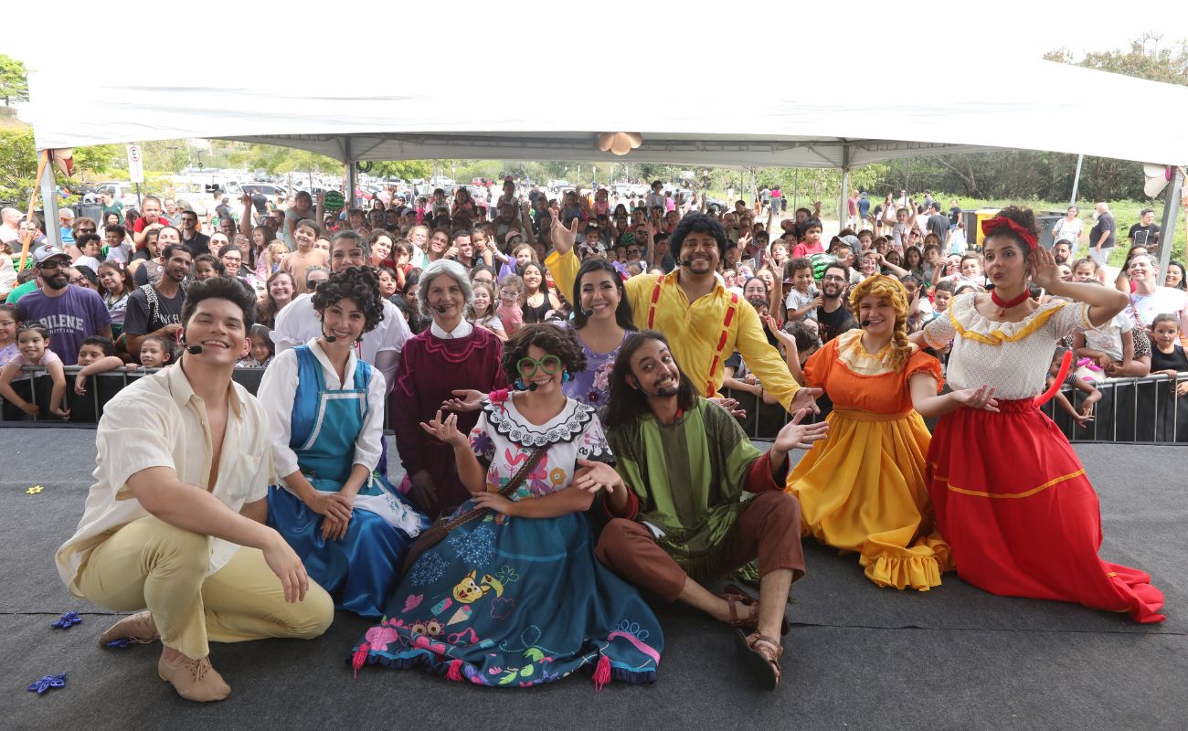 Imagem mostra a equipe de teatro no palco e ao fundo o grande público no evento Manhã das Crianças, como parte da Semana Municipal da Primeira Infância