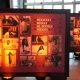 Imagem mostra murais iluminados com fotos de diversas mulheres negras na exposição Mulheres Negras no serviço público