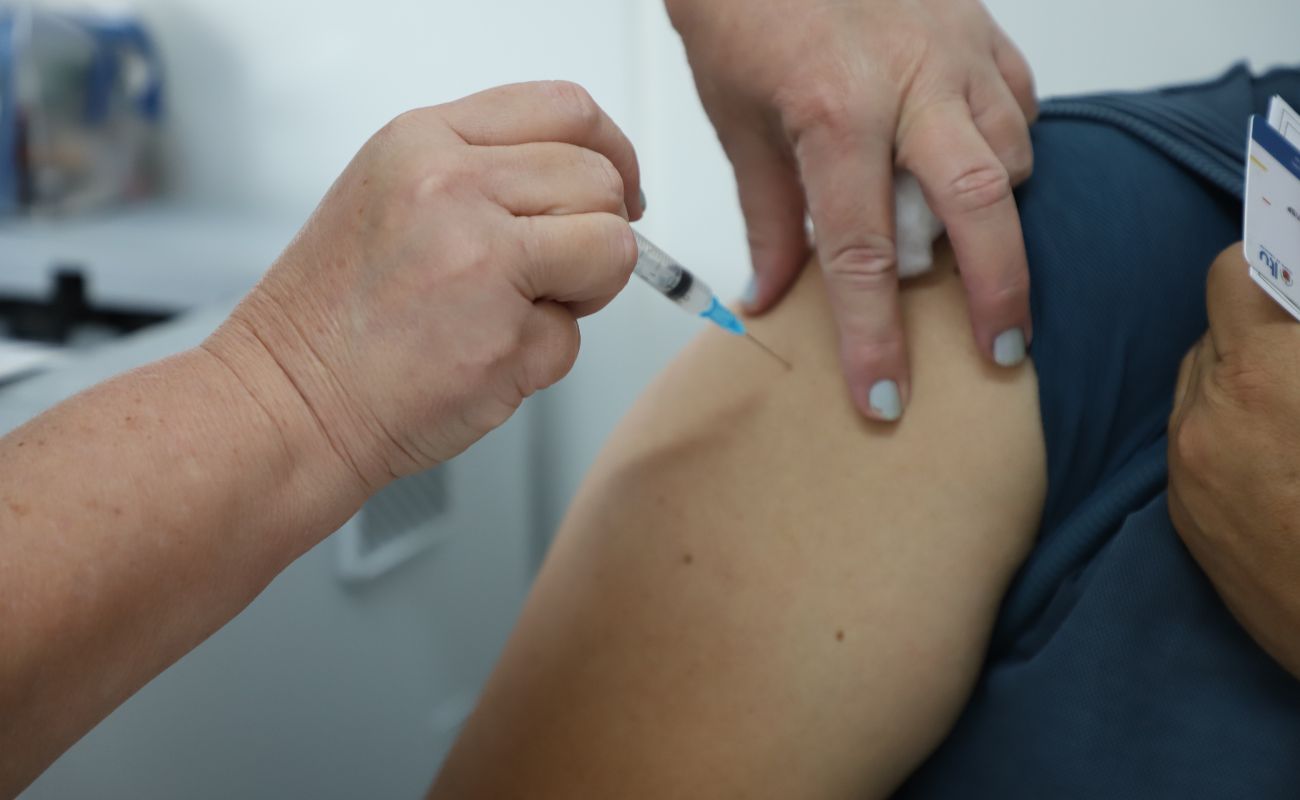 Imagem mostra as mãos de uma enfermeira em foco, aplicando vacina em pessoa