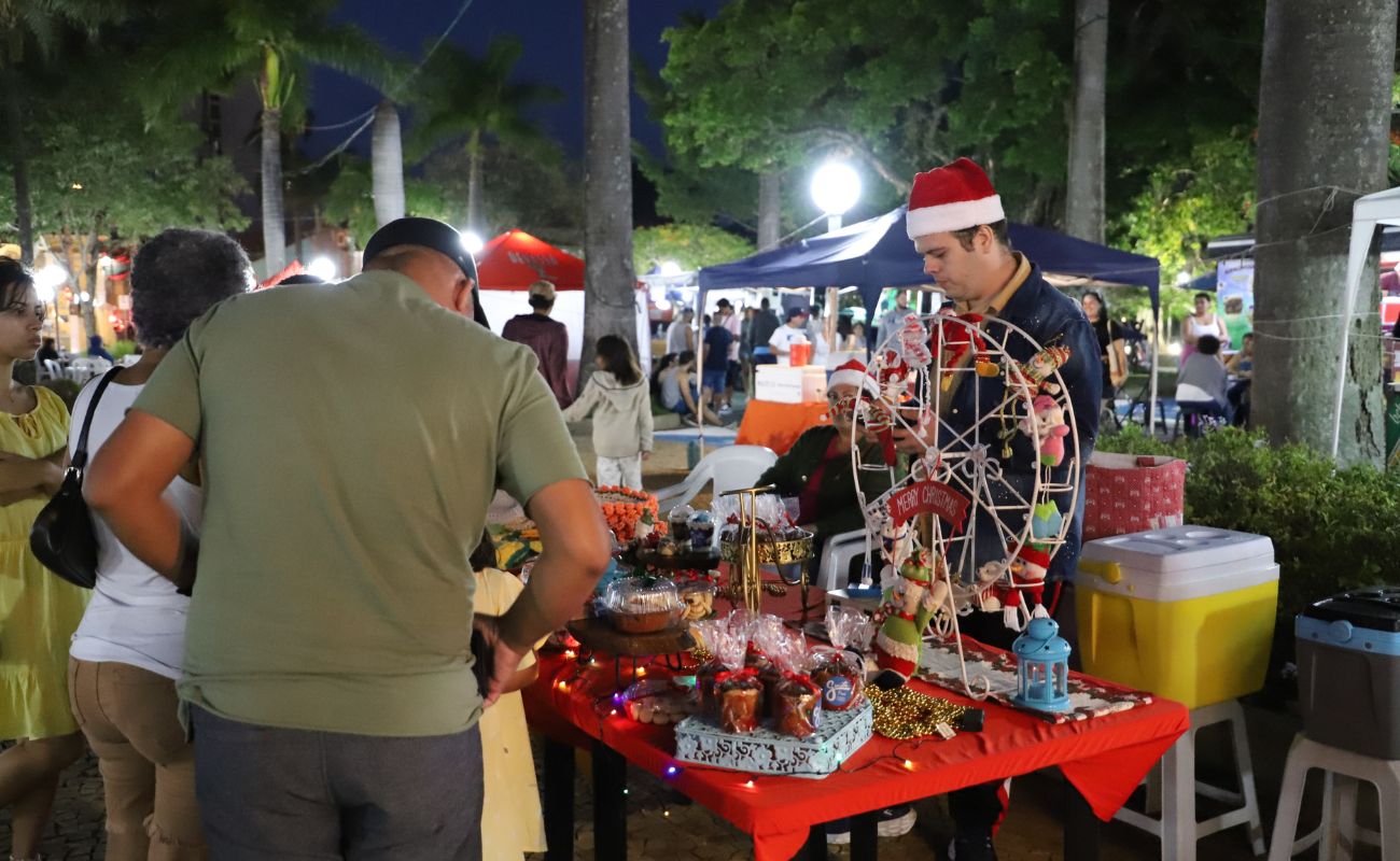 Imagem mostra duas pessoas de costas vendo itens vendidos por um dos vendedores da Feira de Natal.