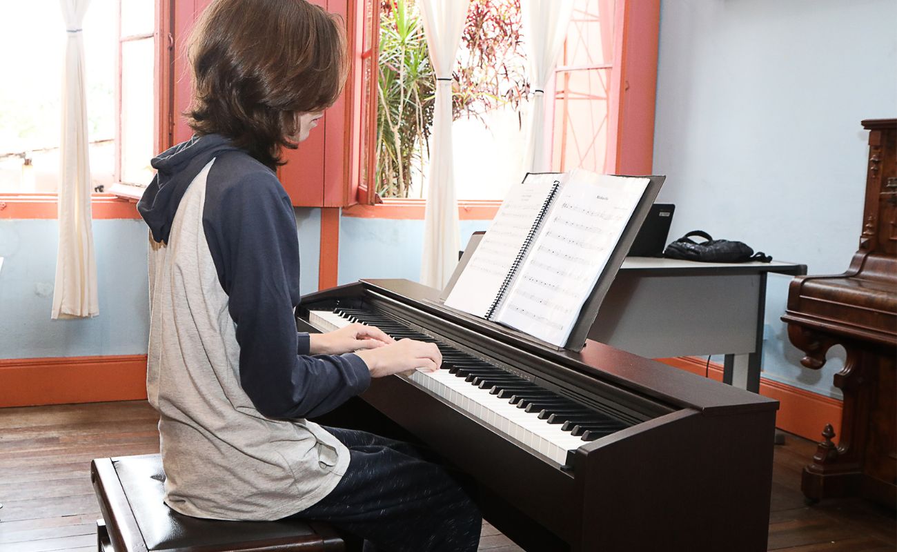 Imagem mostra aluno da Emia em uma aula de piano referente aos cursos artísticos gratuitos oferecidos.