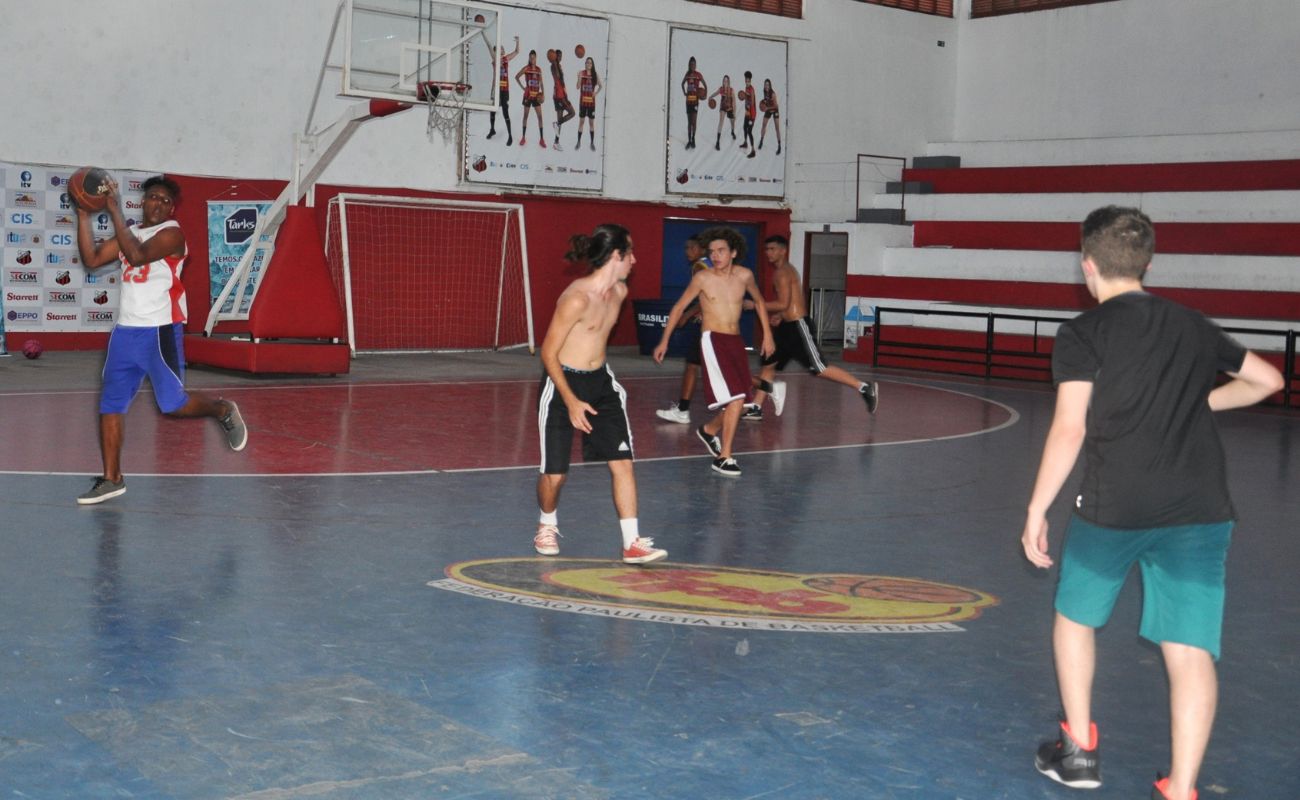 Imagem mostra jovens jogando basquete em quadra esportiva.