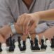 Imagem mostra em foco a mão de um aluno movimentando uma peça durante um jogo de xadrez.