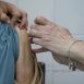 Imagem mostra em foco o braço de uma enfermeira em momento de aplicação de uma das vacinas que correspondem a vacinação, indicadas nesse posto os locais de campanhas.
