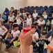 Imagem mostra crianças olhando curiosamente para um copo com líquido vermelho, referente a experimento realizado em uma das ações de promoção do consumo consciente e da preservação ambiental em Itu, durante a Semana da Água em Itu.