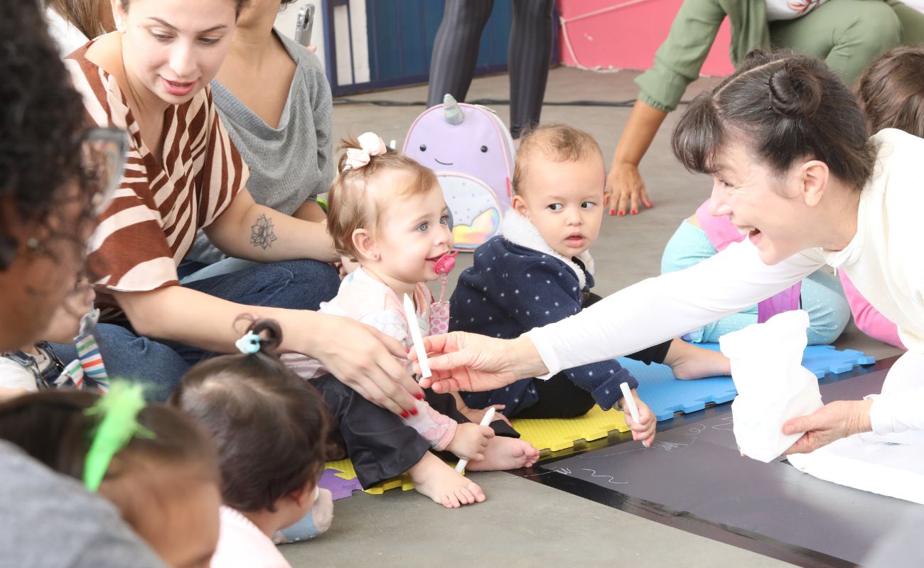 Imagem mostra bebês em momento de interação no palco em apresentação do teatro para bebês, na festa para as crianças.