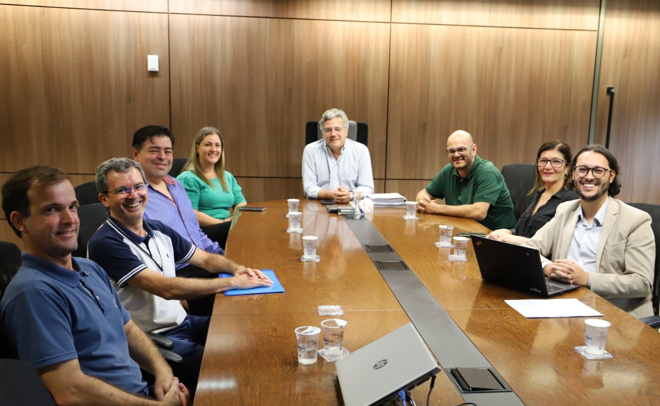 Imagem mostra o prefeito Guilherme Gazzola em sua mesa na sala de reunião do gabinete, junto a sua equipe e autoridades estaduais.