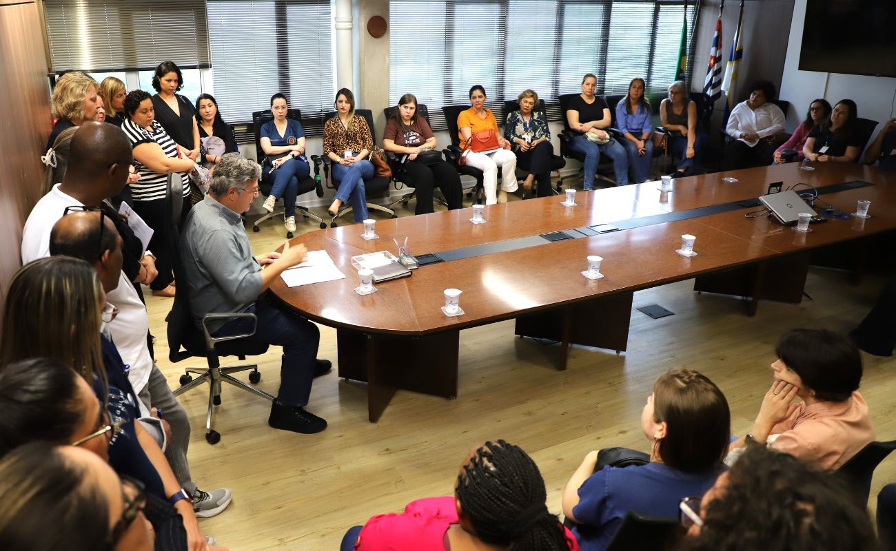 Imagem mostra o prefeito Guilherme Gazzola sentado em cadeira de sala de reunião do gabinete, junto a equipe da Secretaria de Saúde.